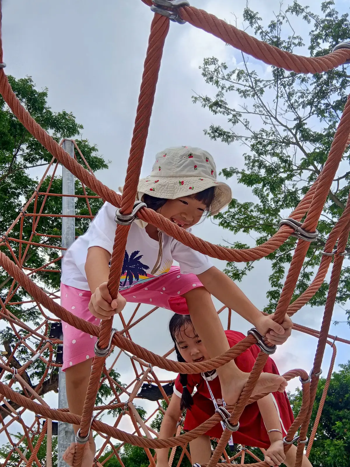 Cảm giác chinh phục khi leo lên đỉnh mạng lưới dây thừng, một bạn nhỏ đang nhìn xuống với nụ cười đầy tự hào.